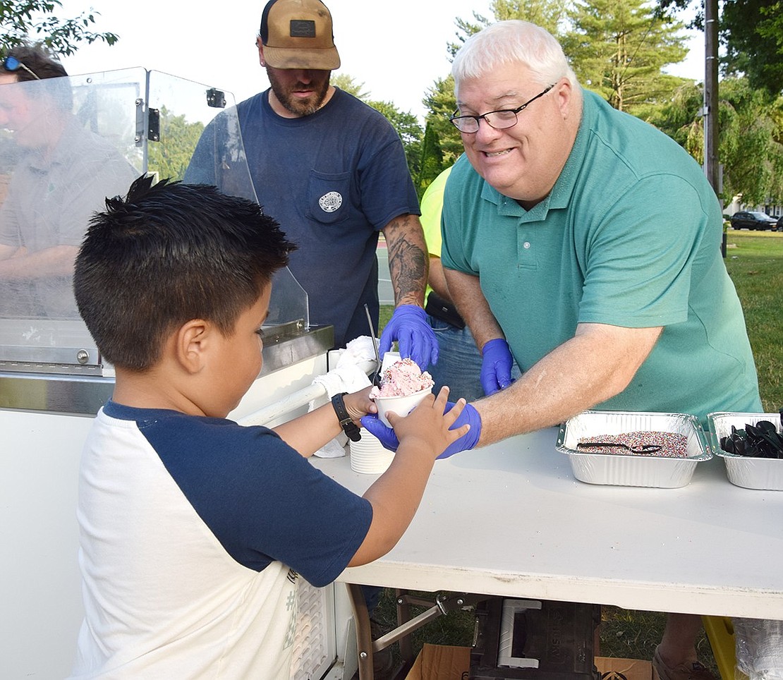 Rye Brook resident Matthew Lopez (left) eagerly accepts a cup of strawberry ice cream from Village Administrator Chris Bradbury.