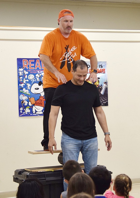 Jester Jim enlists the help of North Regent Street resident Andrew Fernandez to stabilize him as he climbs onto a balancing board for his last stunt of the evening.