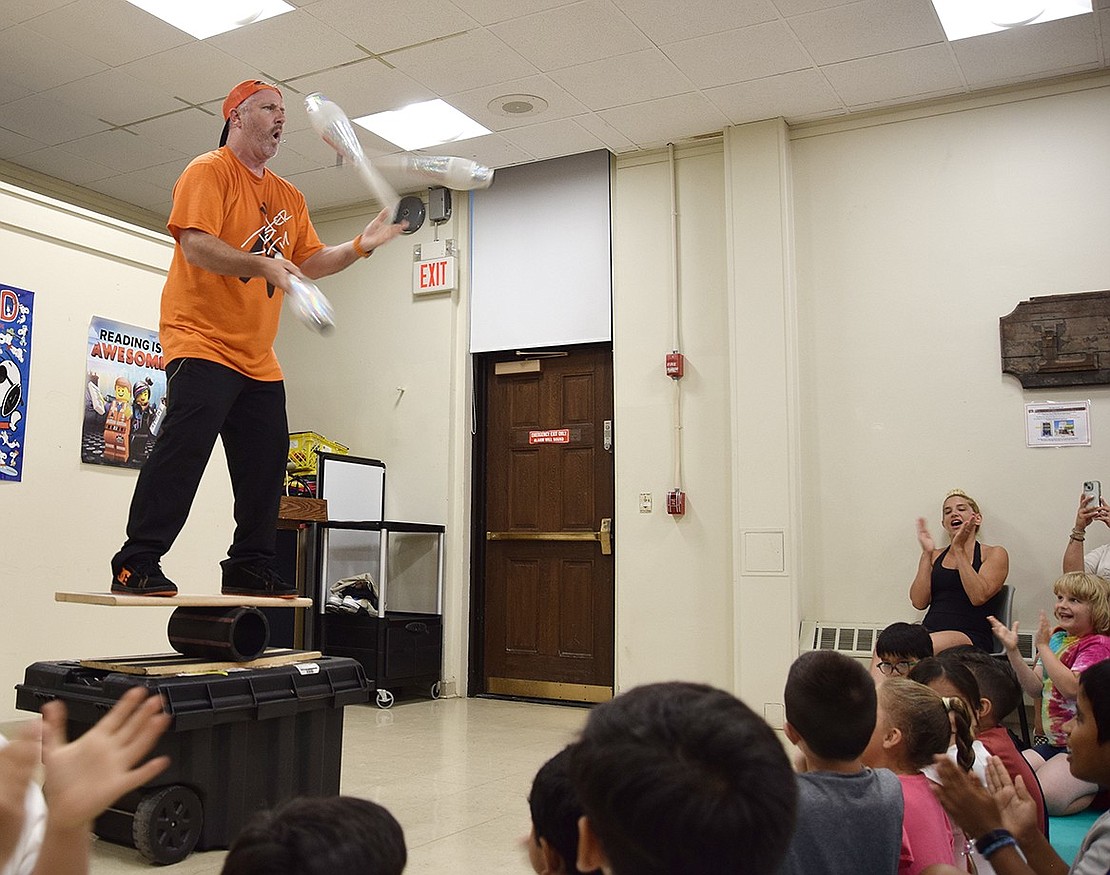 The crowd claps for Jester Jim as he performs his daring final act—juggling three pins while balancing on a rolling platform at the Port Chester-Rye Brook Public Library on July 8. As part of the library’s children’s programming, he was invited to entertain local youth in a variety of ways during an evening of silliness.