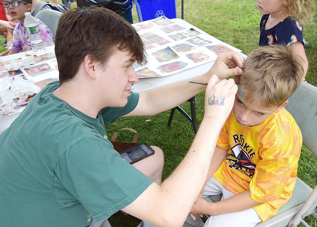 Noah Rotfeld, a 20-year-old Port Chester High School alumnus, uses his phone for reference while painting on 7-year-old Brush Hollow Close resident Jules Francis’ face.