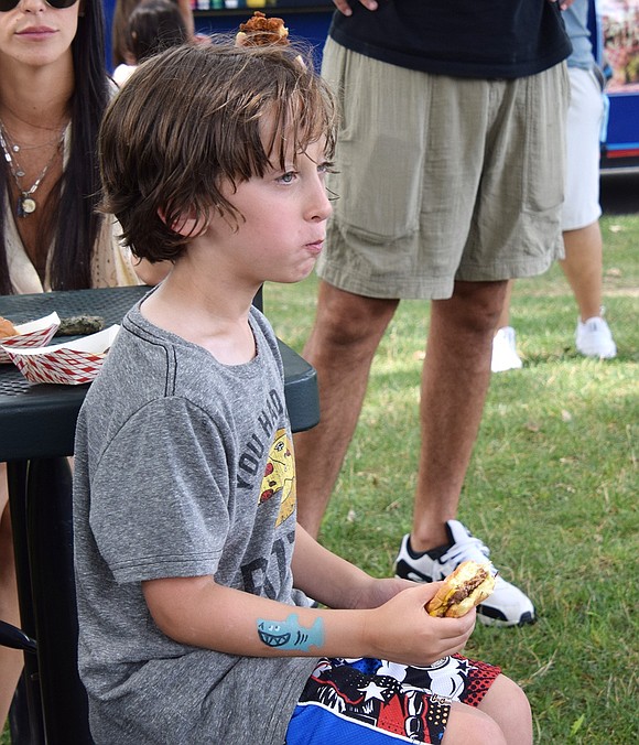 After playing in the park, 6-year-old Parker Tomback, a resident of The Arbors, has a seat to enjoy a cheeseburger from Neil’s on Wheels.