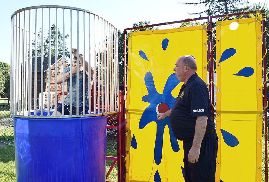 Police Captain Charles Nielsen finds it easier to hit the dunk tank target with his hands to drop Officer Steven Alvarez into the water.