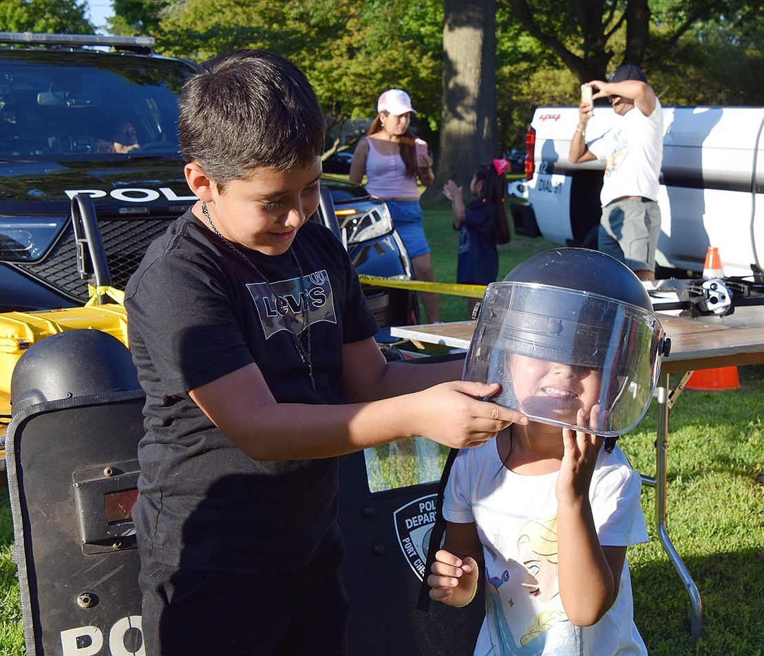 Halstead Avenue resident José Samano, 9, helps Leilani Escobar, 4, try on a police helmet.