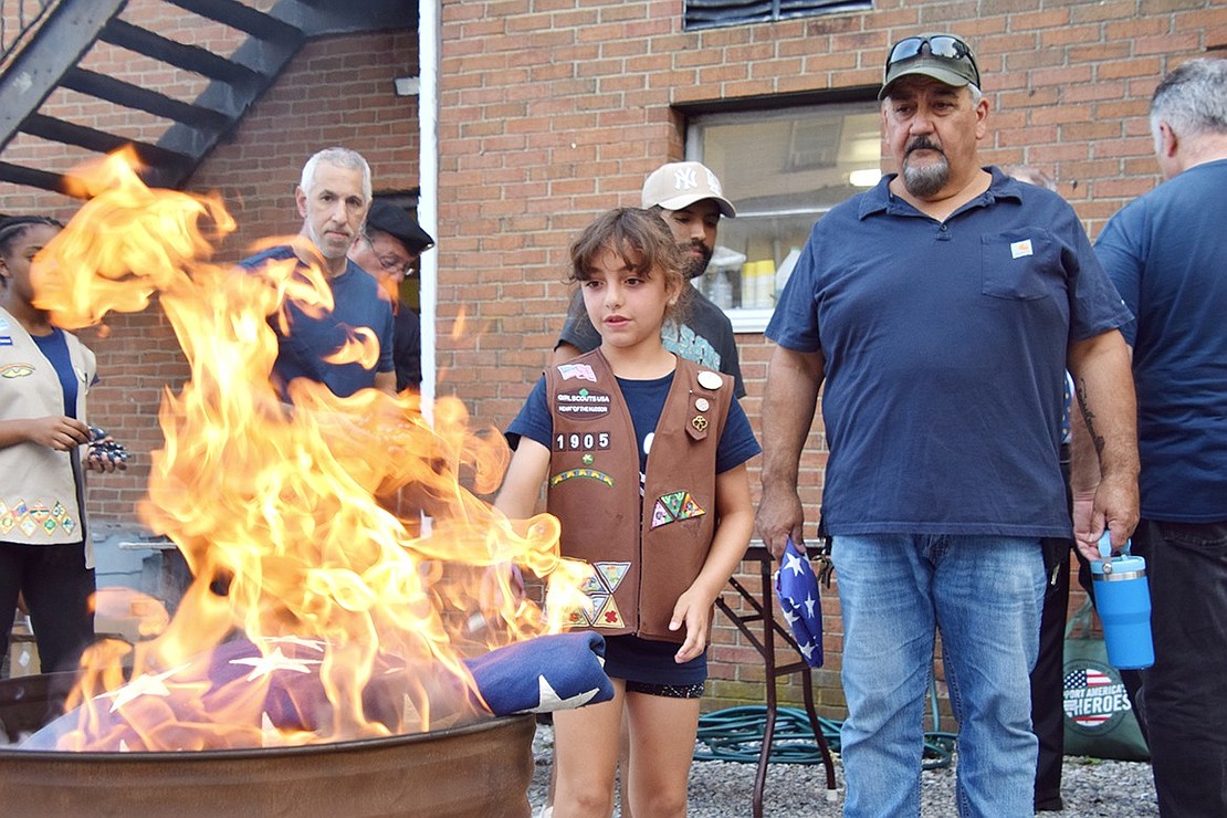 Port Chester resident Sophia Labrusciano, 9, cautiously tosses a flag into the fire, while her father Angelo (right) keeps watch over her.