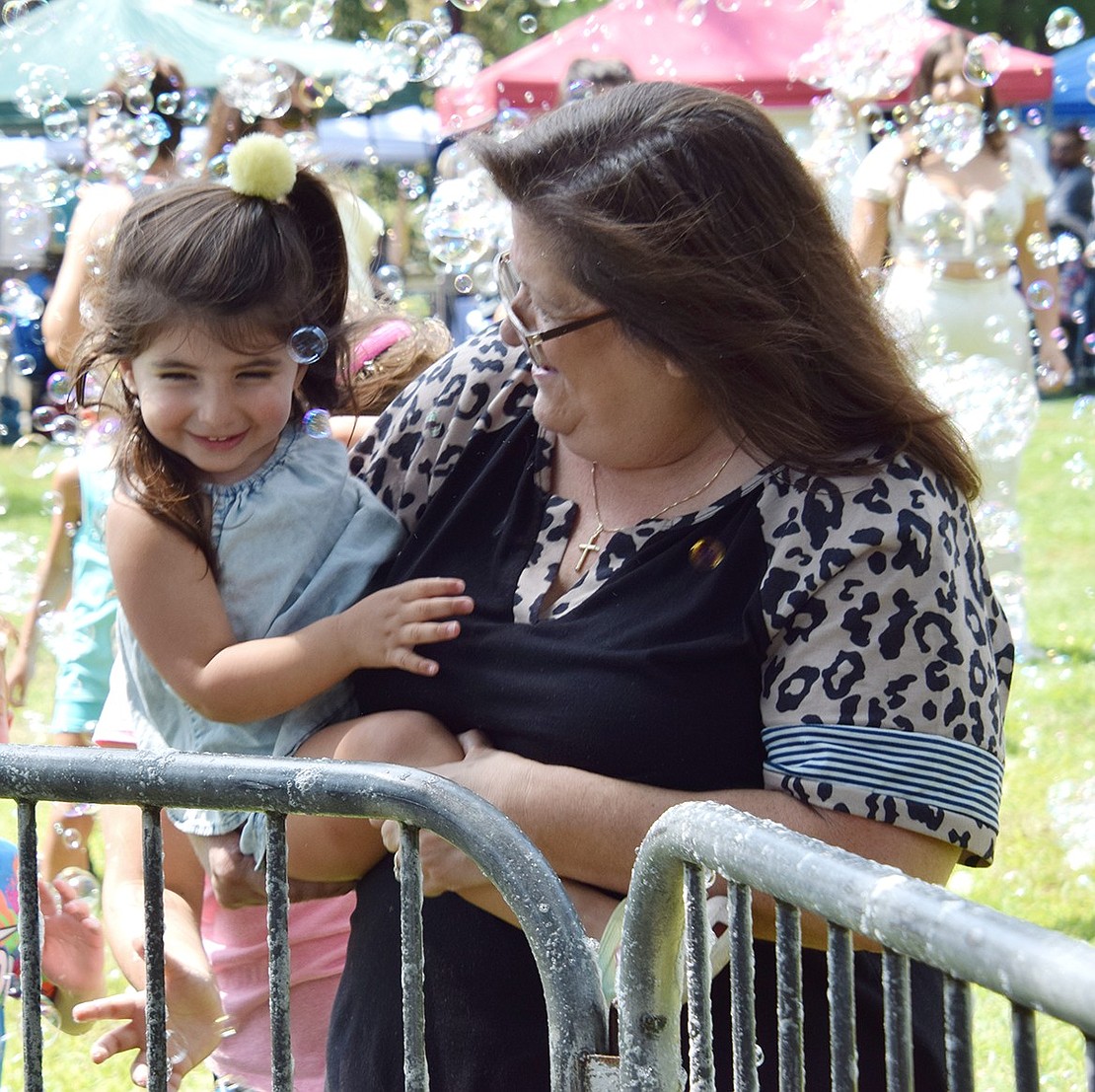 Port Chester resident Violet Gasparino, 2, smiles in the arms of her grandmother Michele Andreoli as they make their way through some bubbles blasting across the park.