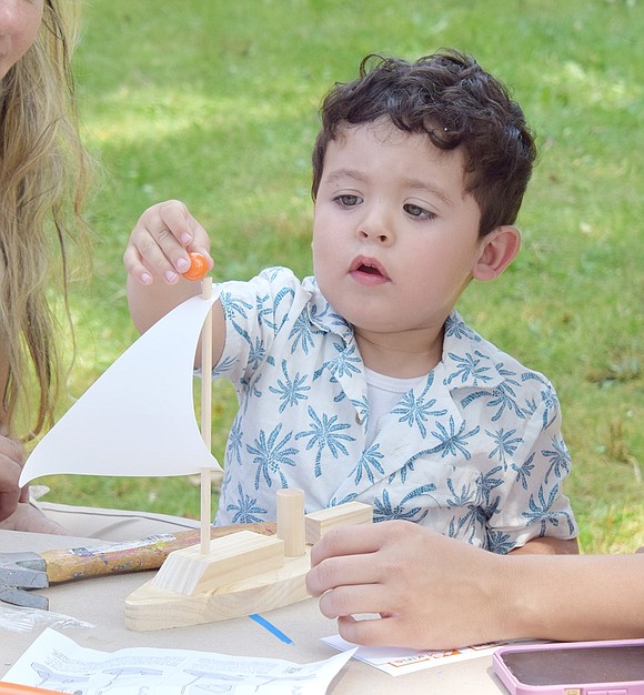 Ismael Reyes, a 2-year-old who lives on Franklin Street, carefully puts the finishing touch on a wooden sailboat he built with the help of his family members, Patricia Reyes and Regina Royo, at The Home Depot arts and crafts table.