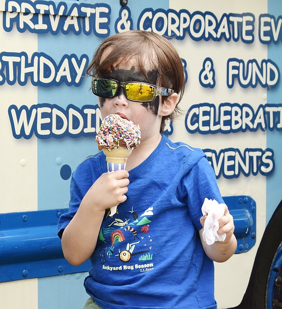 Looking cool with shades over his bat face paint, 4-year-old Halstead Avenue resident Leo Cutler takes a bite of his chocolate ice cream cone covered in sprinkles.