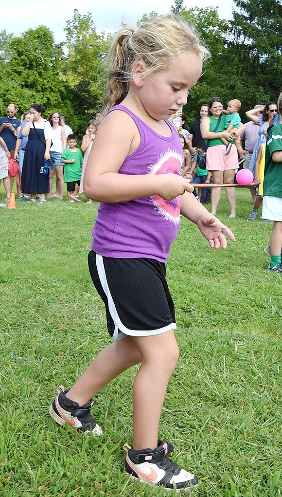 Ruby Noymer goes slow and steady to transport a magenta ping-pong ball on a spoon across the lawn. The egg & spoon race at the Kindergarten Social was a source of great excitement, despite the 90-degree heatwave.