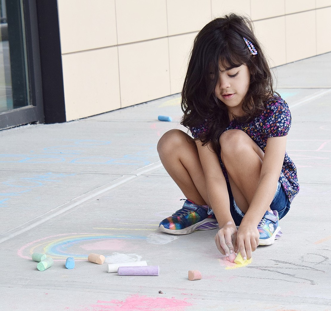 With chalk in both hands, 6-year-old Betsy Brown Road resident Bianca Ciardullo adds to the decorations at Ridge Street School during Chalk the Walk.