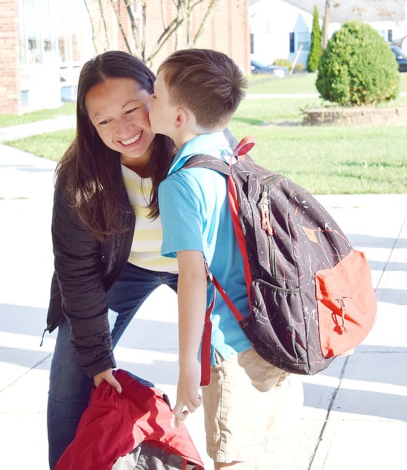 Field Place mom Karen Brown bends down to get a goodbye kiss from her 7-year-old son Logan before he heads into his first day as a King Street School second-grader.