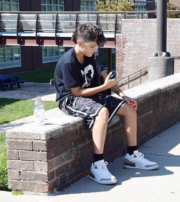 Braden Squillace ends his first day as an eighth-grader at Port Chester Middle School by killing time on his phone as he waits for his ride home on Field Place.