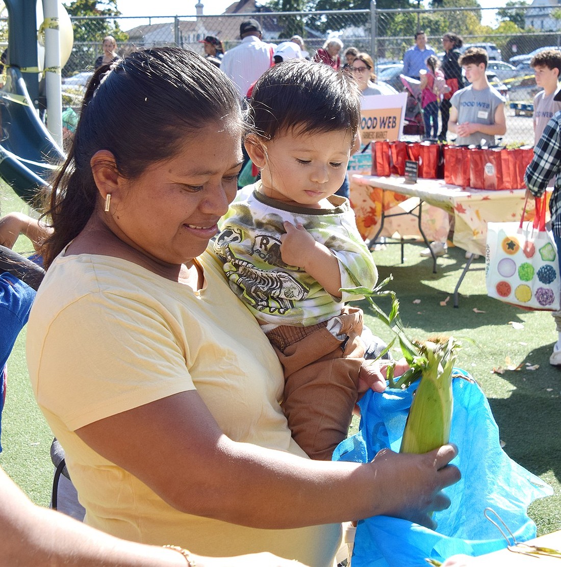 Oak Street resident Milbia Ecal gingerly takes an ear of corn at the Farmer’s Market hosted by the Carver Center on Saturday, Oct. 5, as she carries her 9-month-old son Melvin Lemos. Volunteers and Carver Center employees distributed 5,950 pounds of food to 157 households that day.