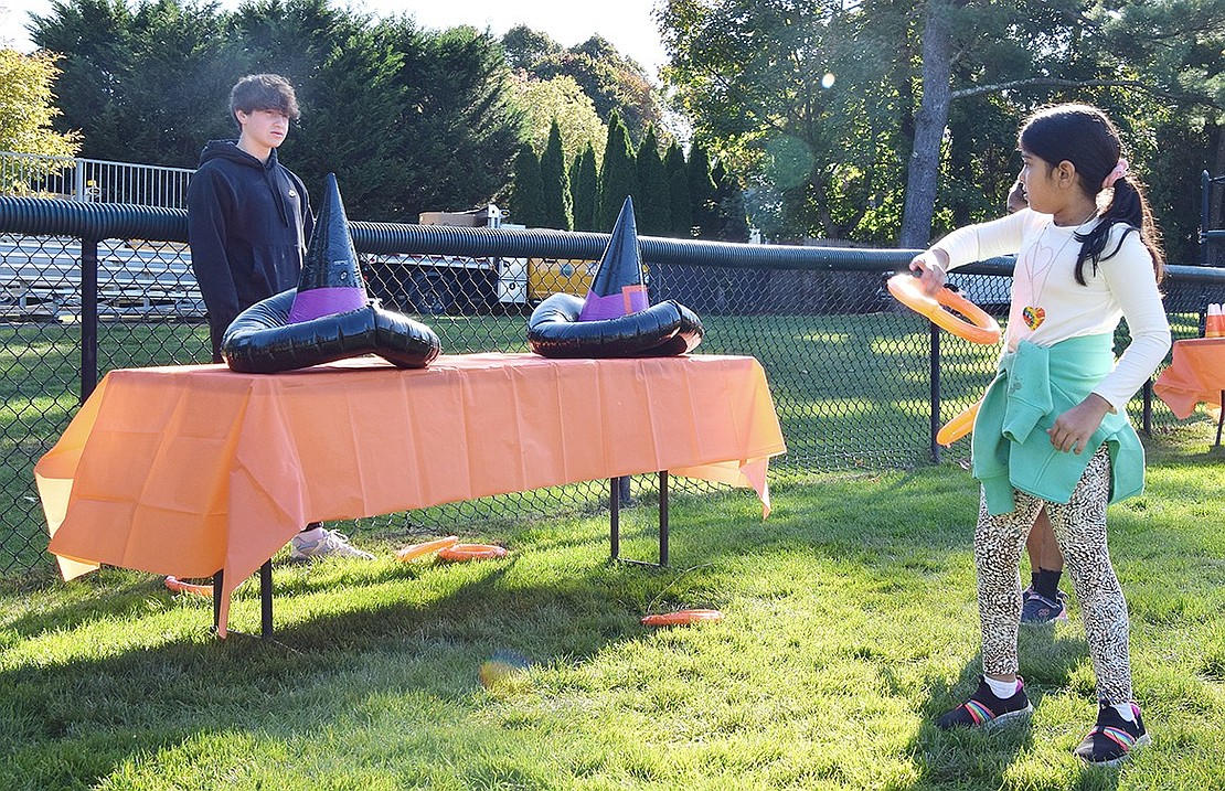 Navya Sivakumar, a second-grader at Ridge Street Elementary School, tries her hand at the witch hat ring toss game, run by Blind Brook High School sophomore Blake Goldstein.