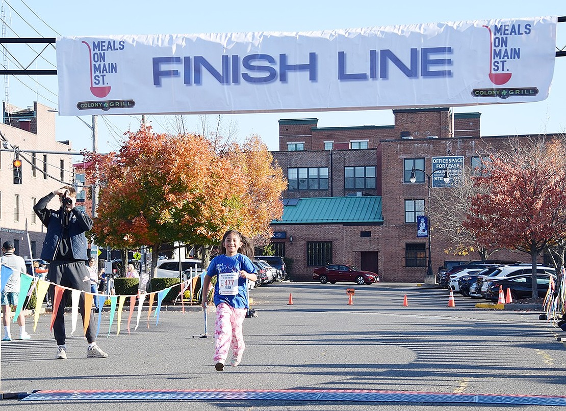 Adee Street resident Angelica Ramirez, 7, smiles widely as she crosses the finish line at the 4th annual Meals on Main Street 5K & Fun Run on Sunday, Oct. 20.