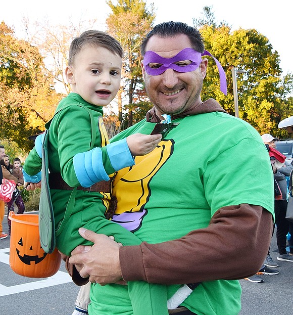 “Happy Halloween,” shouts 3-year-old Jackson Fox and his dad Jason as they walk to the next car for more candy. The father-son duo is dressed as the Teenage Mutant Ninja Turtles Leonardo and Donatello, respectively.