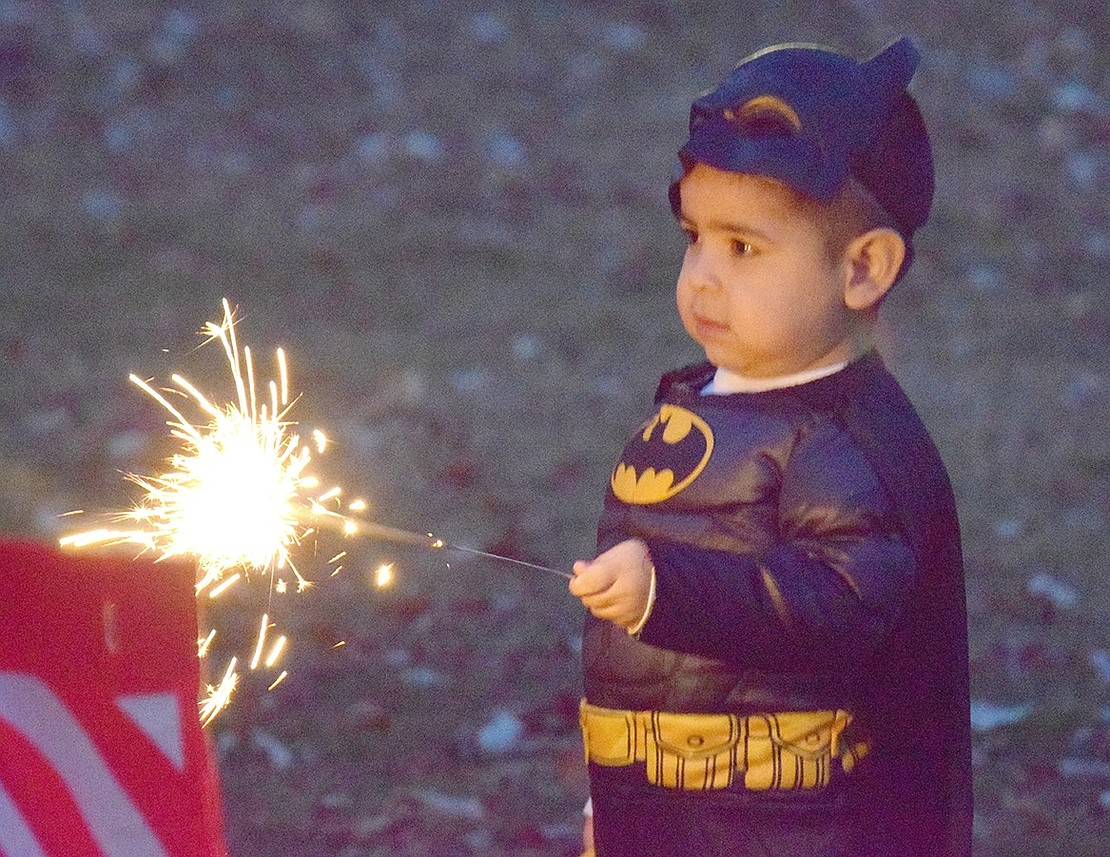 As nighttime falls, Batman uses a sparkler to light up Lyon Park. Jayden Herrera, a 2-year-old Rectory Street resident, is cautiously mesmerized by the flames.