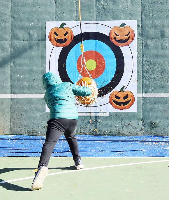 Charles Lane resident AJ Scutero, 9, swings his old pumpkin into the wall using a net system created by DPW employees for the event.