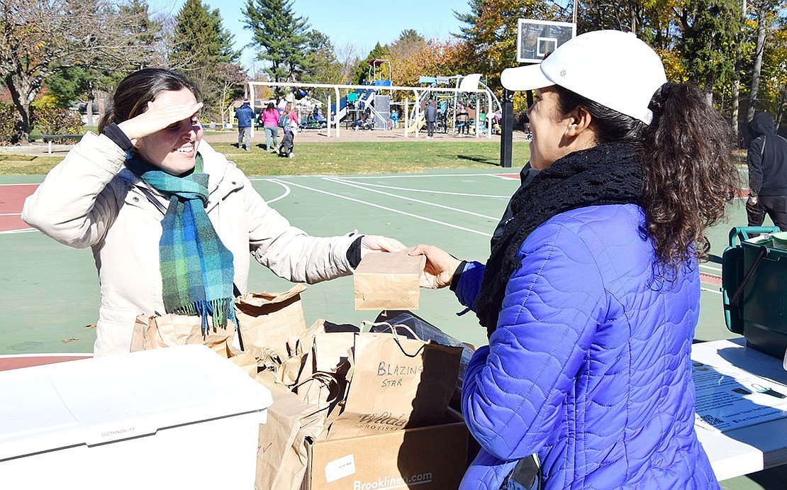 Rye Brook Sustainability Committee chair Brigitte Dix shields her eyes from the sun as she hands a bag of seeds to Hunter Drive resident Alicia Castellano.