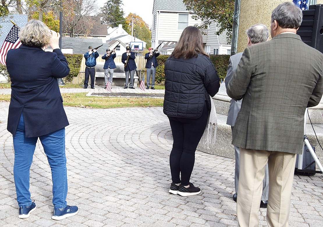 County Legislator Nancy Barr takes a photograph of the firing team, made up of veterans, from left, Ken Neilsen (Vietnam era Navy), Herb Bocchino (Navy), Tom Gallagher (Vietnam era Army) and William P. Sullivan, Jr. (Marine Corps Vietnam) firing shots to honor all veterans. Bugler Anthony Bubbico, Jr. followed with Taps in memory of veterans who have died.