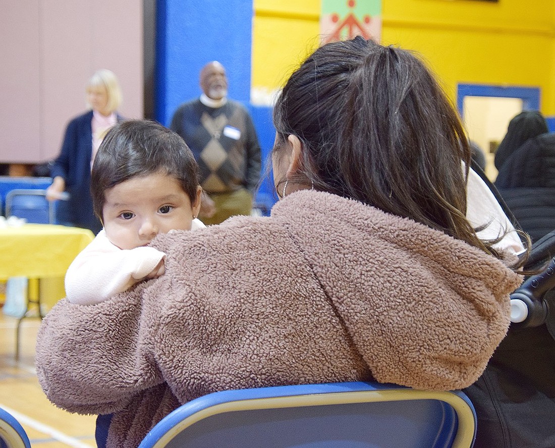 Port Chester 3-month-old Alison Quichimbo is held by her mom, Karen Mollinturo, who listens to members of the Port Chester Immigrant Defense kick off the Community Baby Shower in the Don Bosco Community Center on Saturday, Dec. 7. Residents received information on local resources for new families and care packages donated by the event’s sponsors.