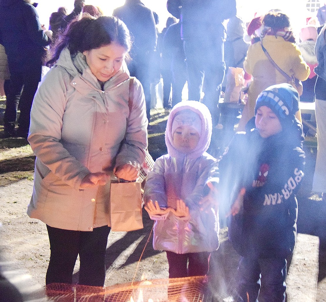 Locust Avenue resident Maritza Polo (left) takes a break from the festivities at the Town of Rye’s Holiday Lights event to warm up at a small fire with her children Emily, 5, and Justin Allcca, 7.