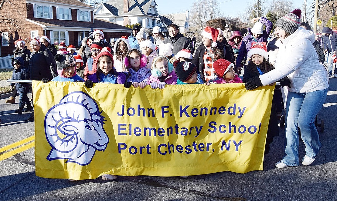 John F. Kennedy Elementary School Principal Colleen Moore (right) helps a group of her students hold up a banner as they march in the Christmas Parade that proceeded down King Street before the Santa in the Park event.