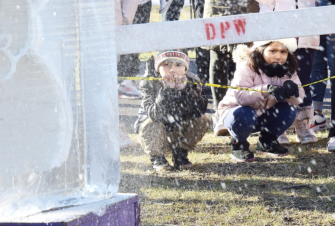 Port Chester residents Kedyn Peraza, 6, and Sofia Lucero, 5, watch the ice carver from below the barrier set up around him.