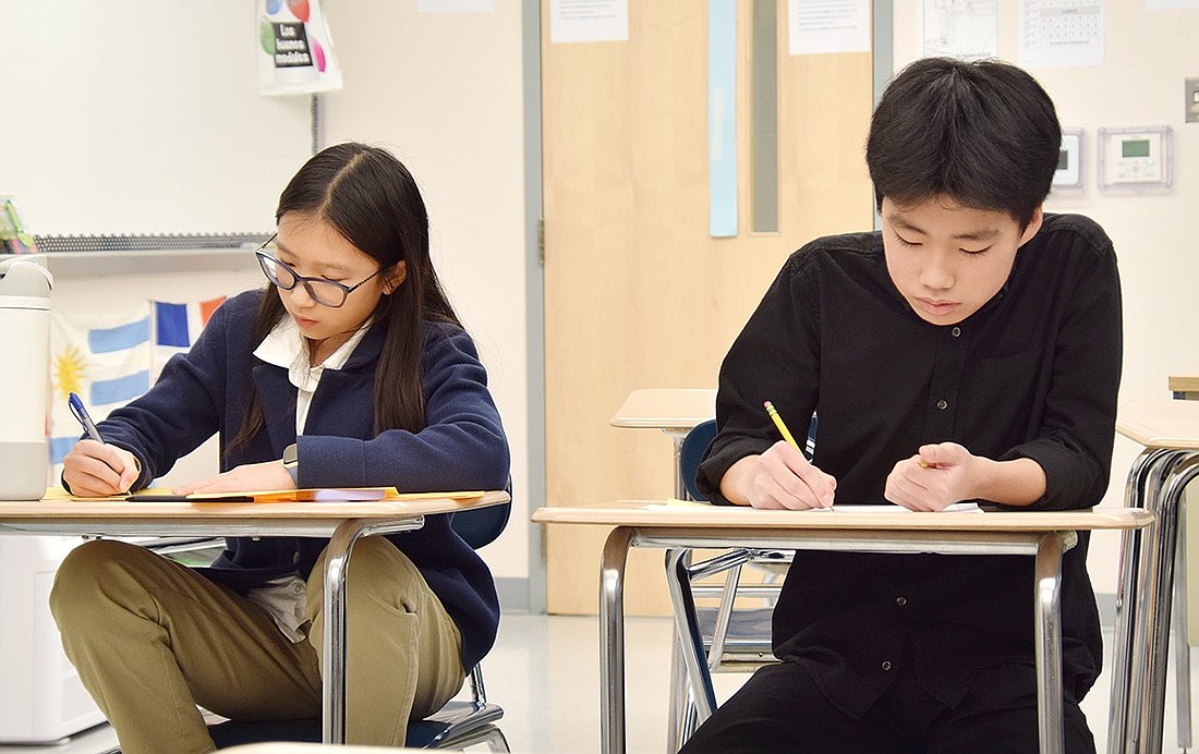 Blind Brook Middle School seventh-grader Jaime Chen (left) and eighth-grader Seima Kitano, two members of the Debate Team, take notes as their opponents address the judge during the fourth round at the first competitive tournament hosted in their district on Saturday, Dec. 14.