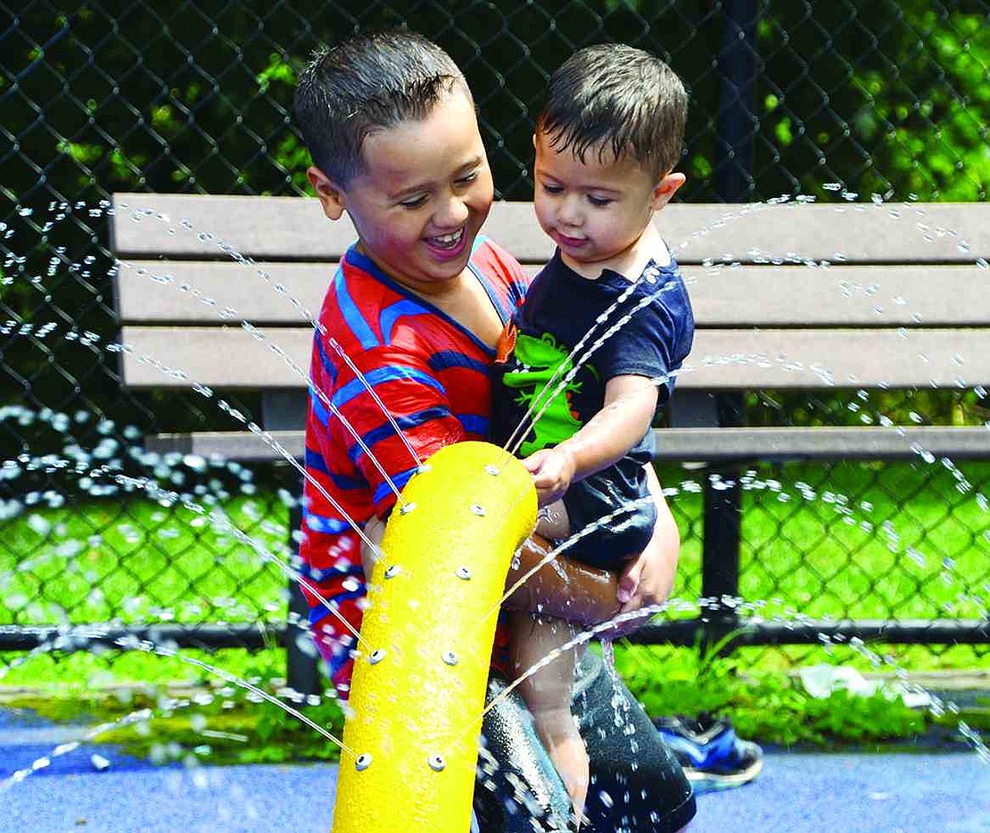 Seven-year-old Ismael Cruz of Purdy Avenue hold up his 1-year-old brother, Xavier Montero, so he can play in the water at the spray park. 