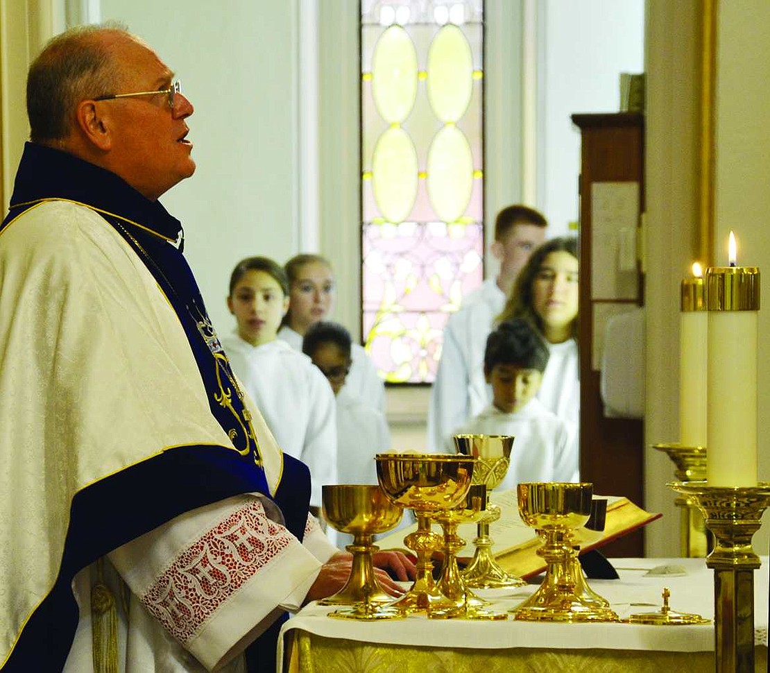 Cardinal Dolan prays over the Holy Eucharist while the altar servers wait in the background.