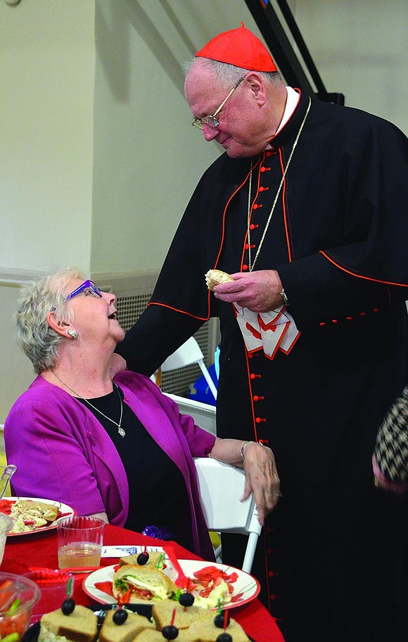 Sandwich in hand, Cardinal Dolan speaks with Margaret Watson of Westchester Avenue during the reception following Mass. 