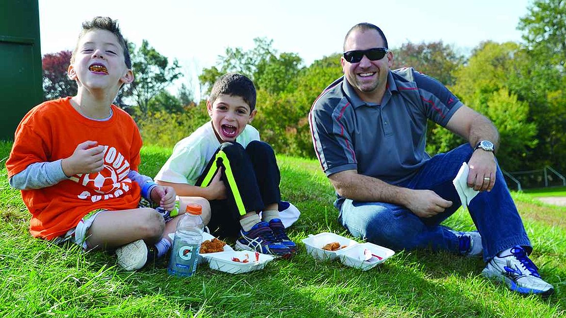 Six-year-olds Charlie Zellman (left) and Matthew Rigano sit on the hill with Matthew's father, Craig, to snack on chicken fingers and listen to the live music. 