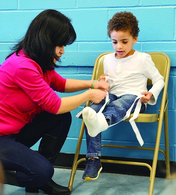  Using a helpful device, Dan Zhu aids kindergartner C.J. McCreath in pulling a sock onto his foot without having to bend down. 