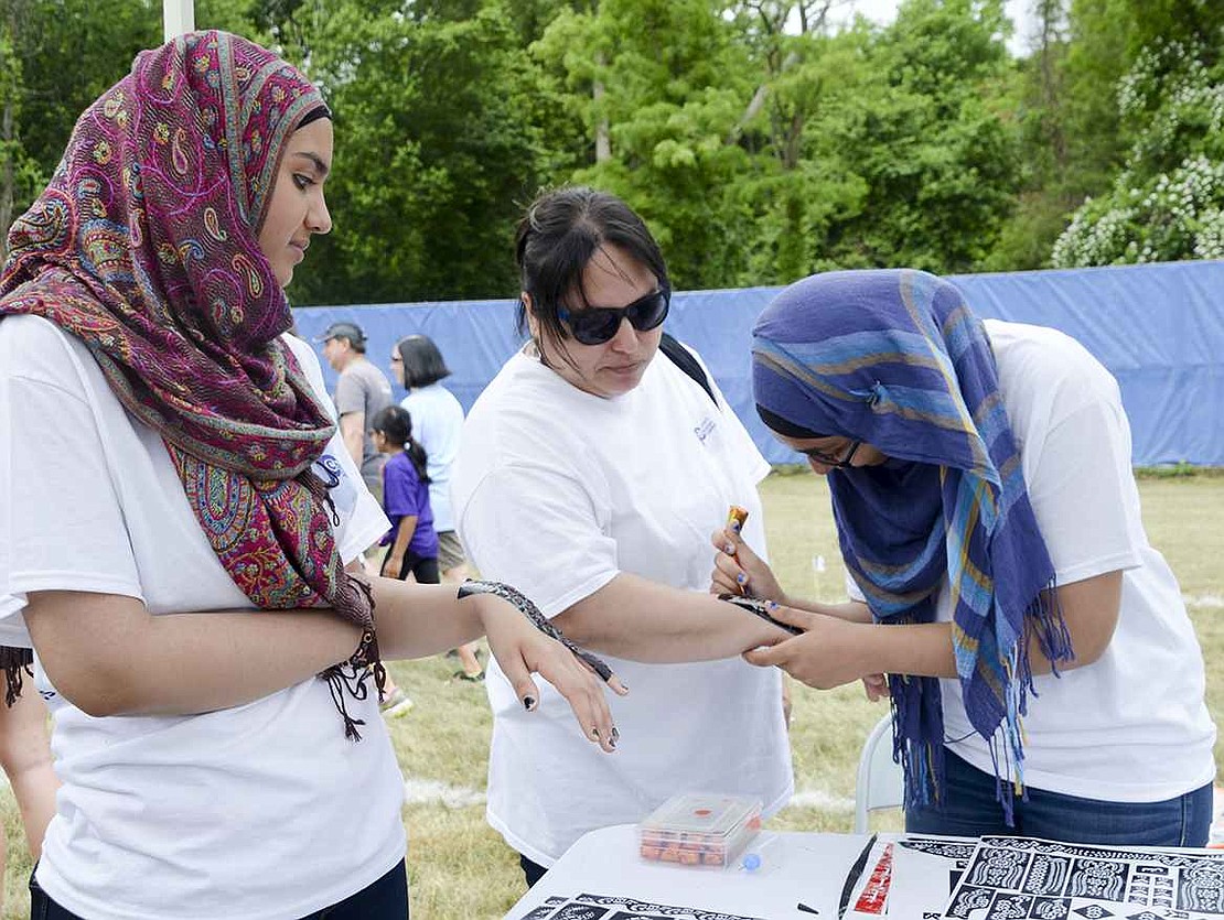 Waiting for the henna on her hand to dry, Mesha Iqbal (left), an 11th grader at Port Chester High School, watches as her sister Larabe (right), a 10th grader, carefully colors in a stencil to leave behind a henna tattoo on Port Chester resident Marianela Payan's arm. 