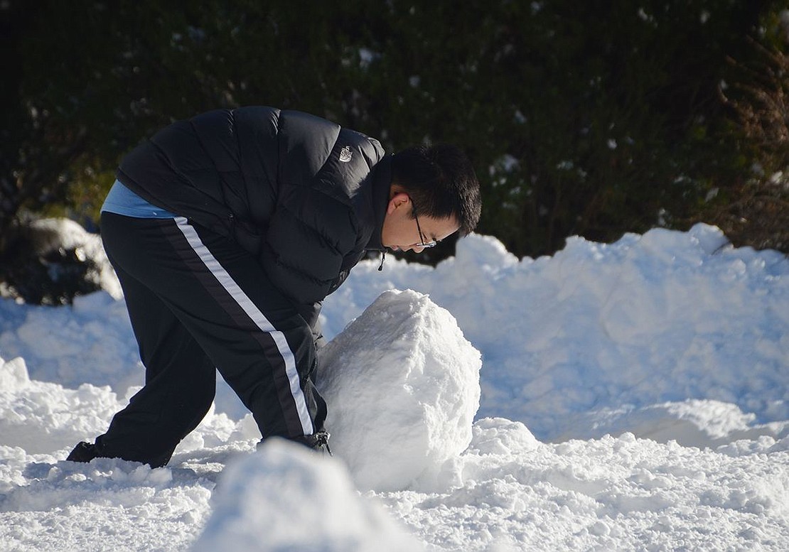 Owen Xie, 16, rolls a huge snowball for a snowman in his front yard at 62 Valley Terrace on Sunday, the day after the storm.