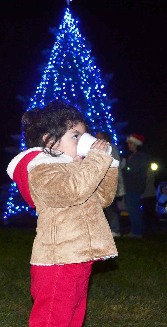  Standing in front of the lit Christmas tree, 2-year-old Alexandra Maldonado of Orchard Street enjoys a cup of cocoa. 