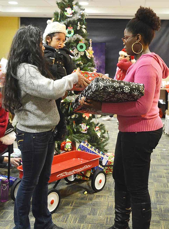  Edwina Iroakazi (right) hands out gifts to mother and daughter. The former AmeriCorps member returned to Open Door to volunteer her time for the holiday event. 