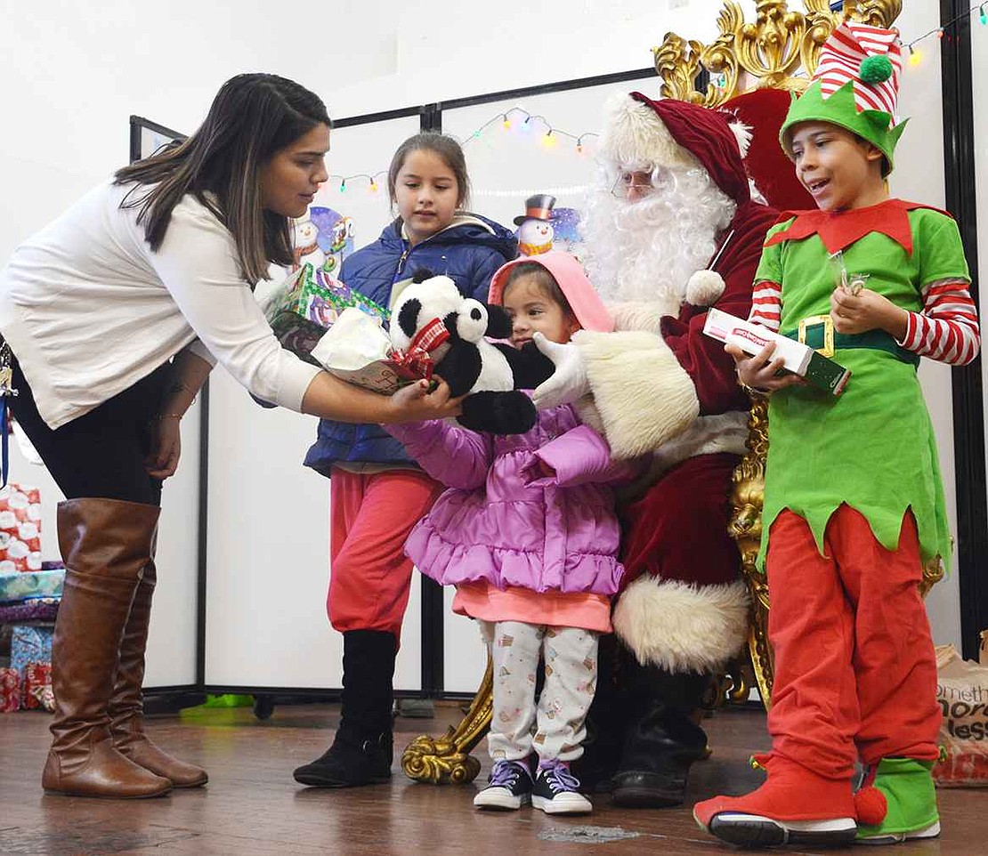  Denise Martinez (left) of Port Chester volunteered her time on Saturday morning to pass out the free, donated gifts to the many children who showed up to the Don Bosco Center, as did Nick Mecca of Port Chester, aka Santa, and 10-year-old Nicholas Santiago Massa of Port Chester, aka his elf.