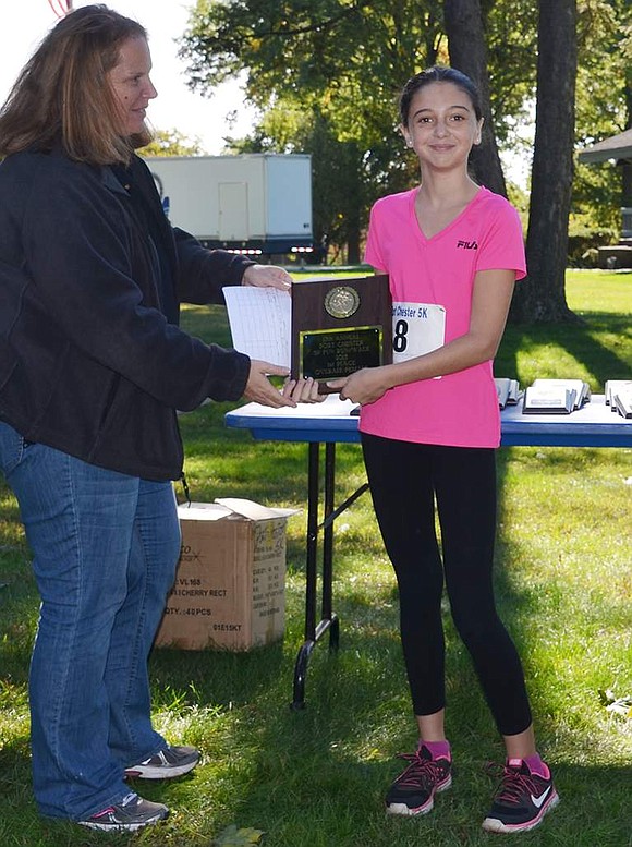 Eleven-year-old Ava Quartarolo of Hobart Avenue accepts a plaque from Heather Krakowski, the Port Chester recreation supervisor. With a race time of 28 minutes and 42 seconds, Quartarolo was the first woman to finish the 5K.