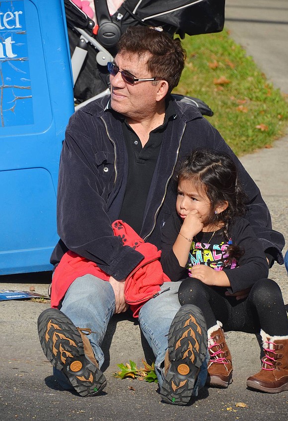 <span style="font-family: Arial;">Leonidas Estrada and daughter Ana of Port Chester watch the parade together seated on the curb.</span>