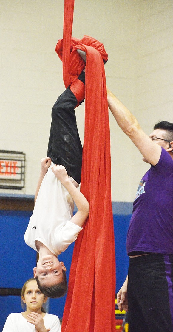 <p class="Picture">Only two boys were brave enough to take on ribbon dancing. Makayla Dutra, with the help of Doug Young, flashes a large smile as he hangs upside down. Fourth graders performed their new skills for their classmates and parents with the help of Doug Young from Circus Kid Productions on Friday, Dec. 9. The students practiced all week during their gym classes to learn how to walk tightropes, balance on balls, juggle and more.&nbsp;</p> Photo story by Casey Watts