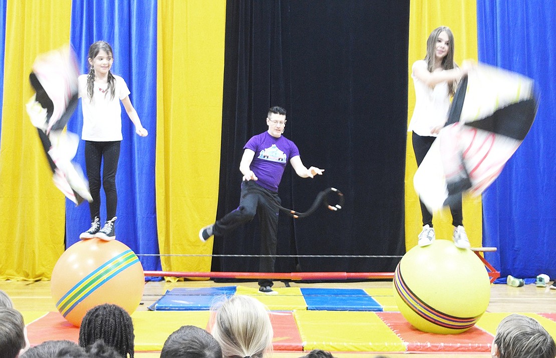 <p class="Picture">Eva Loor-Steinberg and Ella Mensch wave flags while they stand on giant circus balls. In the background, Doug Young prepares for the next trick.</p>