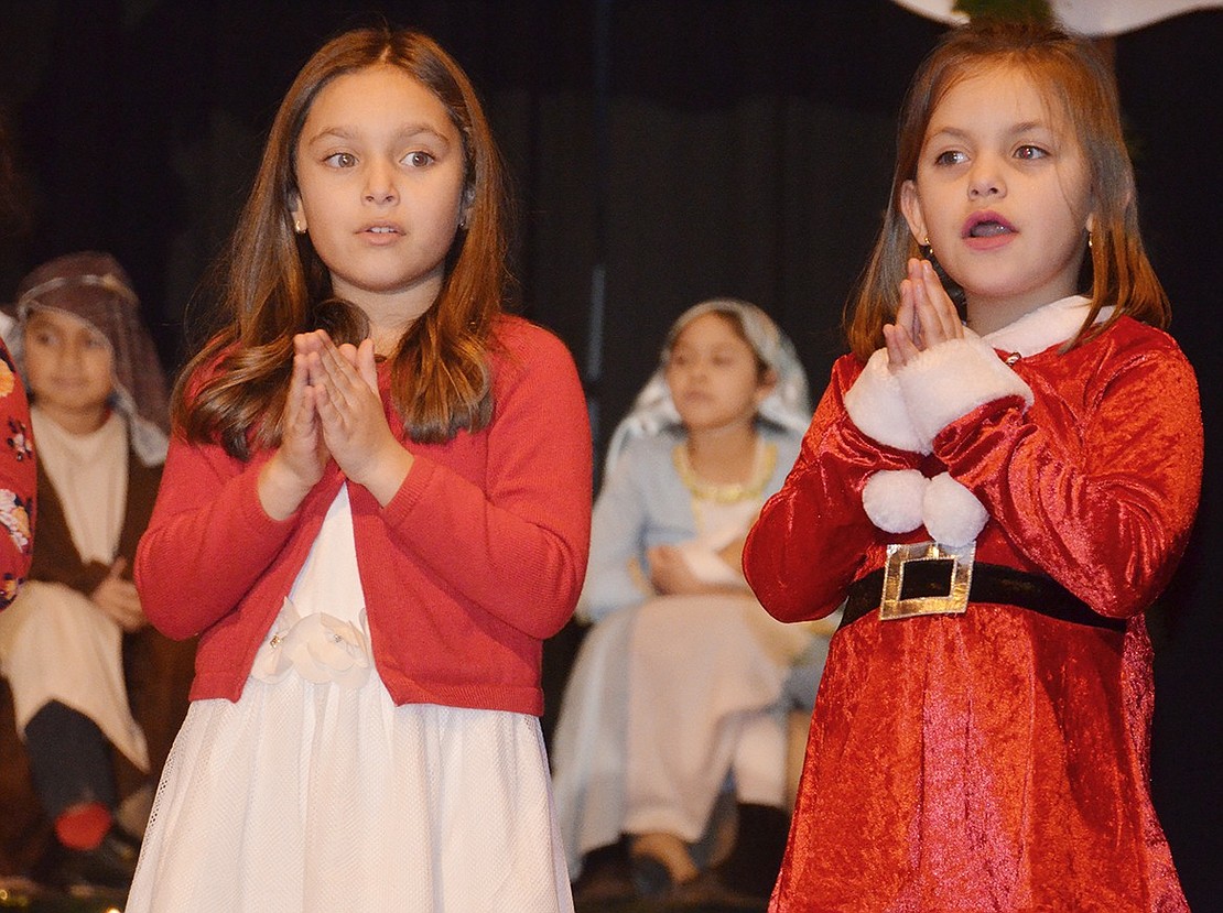 <p class="Picture">First graders Angelina Aiello and Aliza DaSilva hold their hands together in praying position as they sing &ldquo;Silent Night&rdquo; with Mary (second grader Alessandria Rasile) and Joseph (second grader Daniel DeLeon) and Baby Jesus in the background.&nbsp;</p>