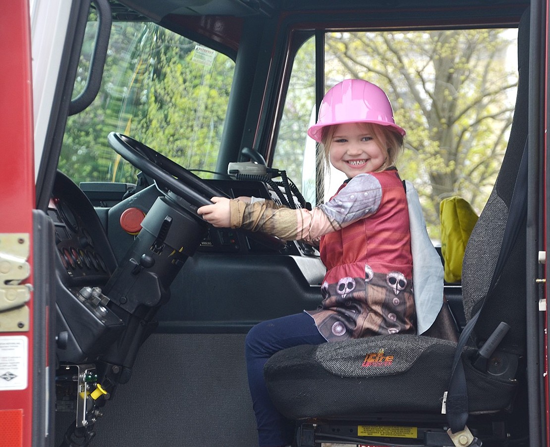 Four-year-old Molly Williams is all smiles in the driver’s seat of a Rye Brook fire engine on Truck Day at Bright Horizons at BelleFair on Apr. 27. Members of the village’s Department of Public Works bought several pieces of equipment to the parking lot of the nursery school that afternoon for the preschoolers to test drive.