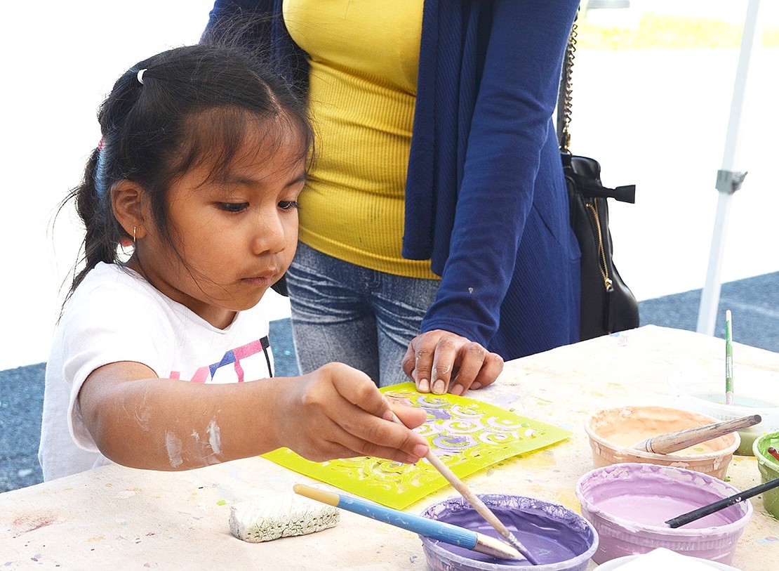 Four-year-old Emily Sigua of Port Chester enjoys painting a tile with colorful blue and purple swirls. 