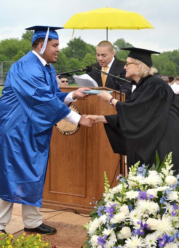 Isaiah Quiroz receives his diploma from Port Chester school board member Anne Capeci while Assistant Principal Juan Sanchez, shielded from the rain by an umbrella, reads the name of the next graduating senior.