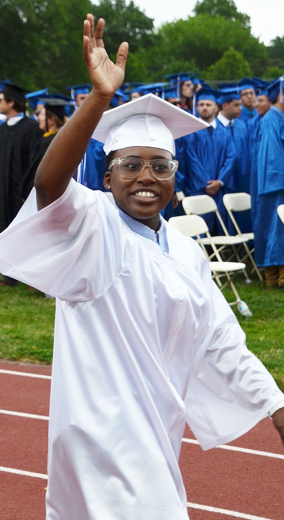 Diamond Scott waves to friends and family in the stands as she walks along the track toward the field to the sounds of “Pomp and Circumstance” by the Port Chester High School Concert Band.