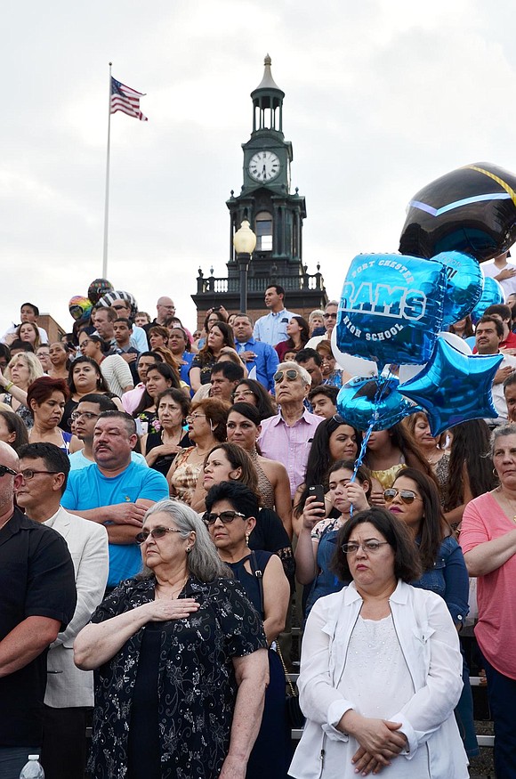 With the clocktower in the background, audience members stand for the National Anthem.