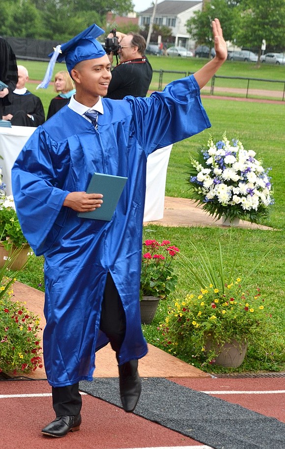 Graduating senior, diploma in hand, waves to the audience.