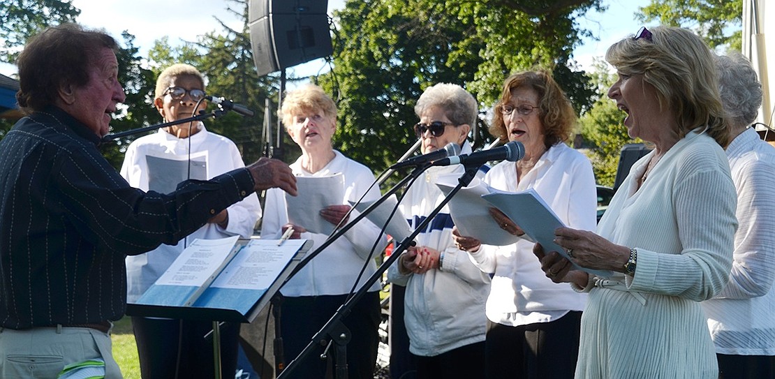 The Port Chester Seniors Chorus, under the direction of Ang Rubino, sing for the crowd gathered on the lawn in front of the village’s Showmobile.